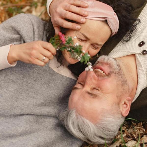 Senior couple lying together on their backs and hugging in a park.