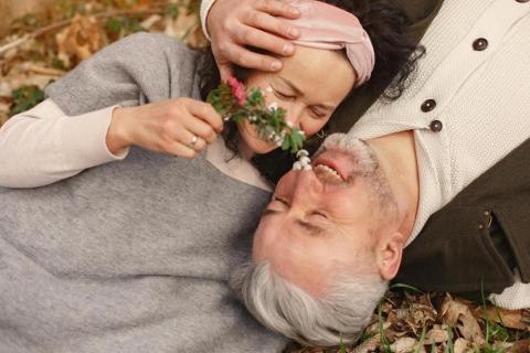 Senior couple lying together on their backs and hugging in a park.