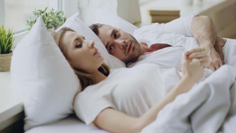 Man lying awake next to his partner, reflecting anxiety and relationship concerns associated with premature ejaculation.